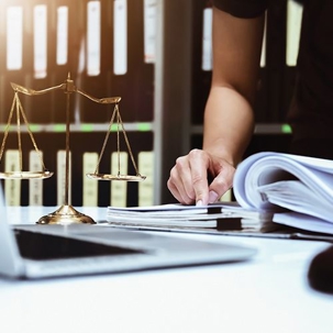 a person sorting through documents, weighing scale of justice and laptop on the table